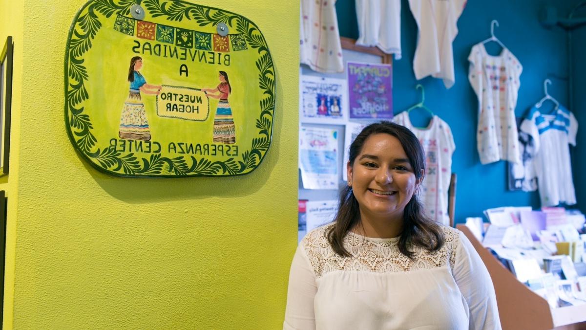 Student smiles in front of a sign at Esperanza Center that reads "bienvenidas" 